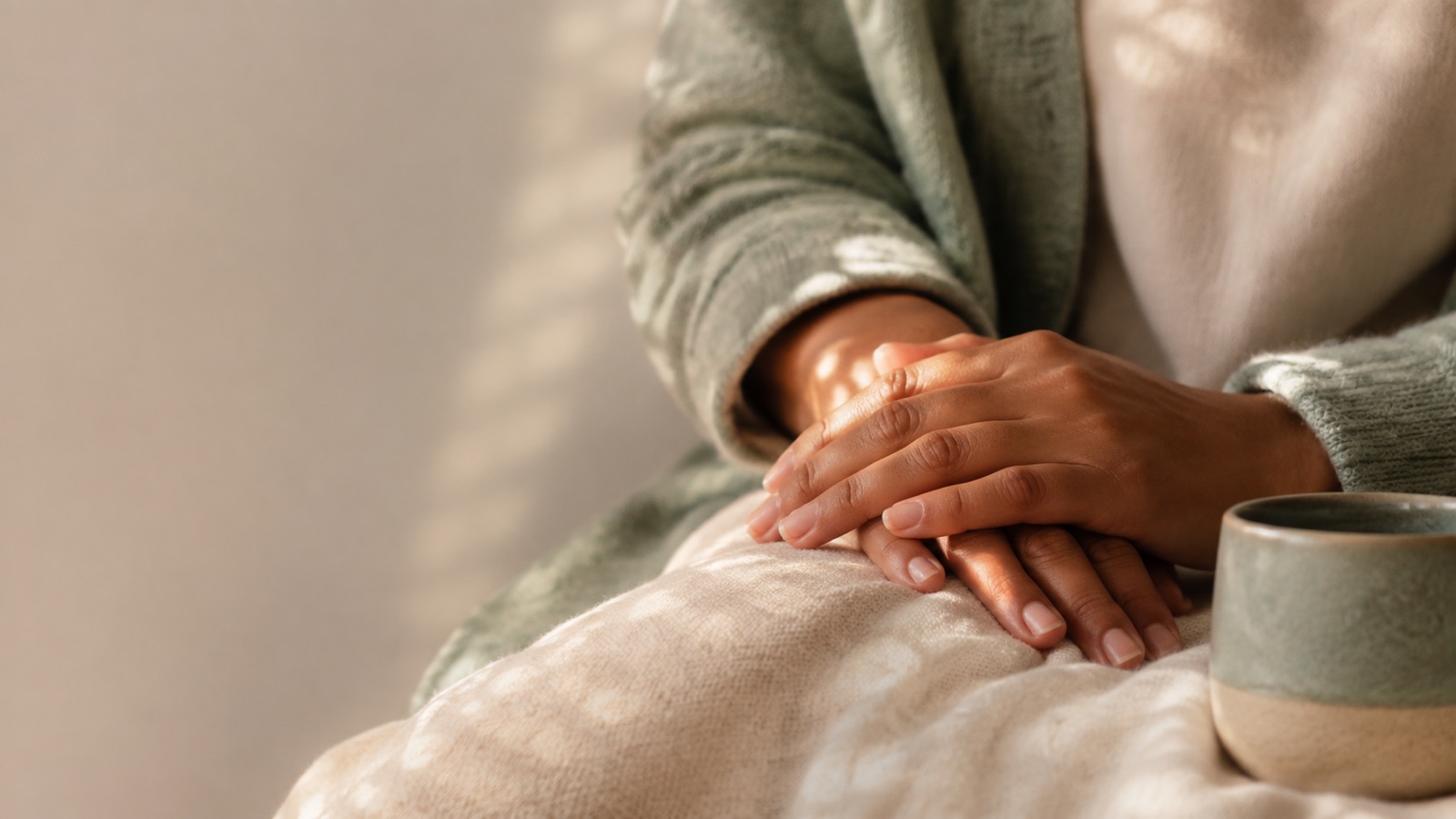 Hands resting calmly on a soft blanket beside a ceramic mug